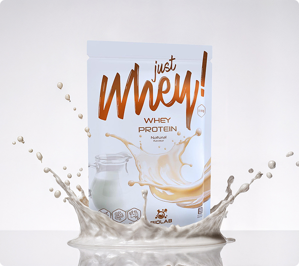 Just Whey Natural 1 kg pouch immersed in a dynamic splash of white, milk-like liquid on a light background.